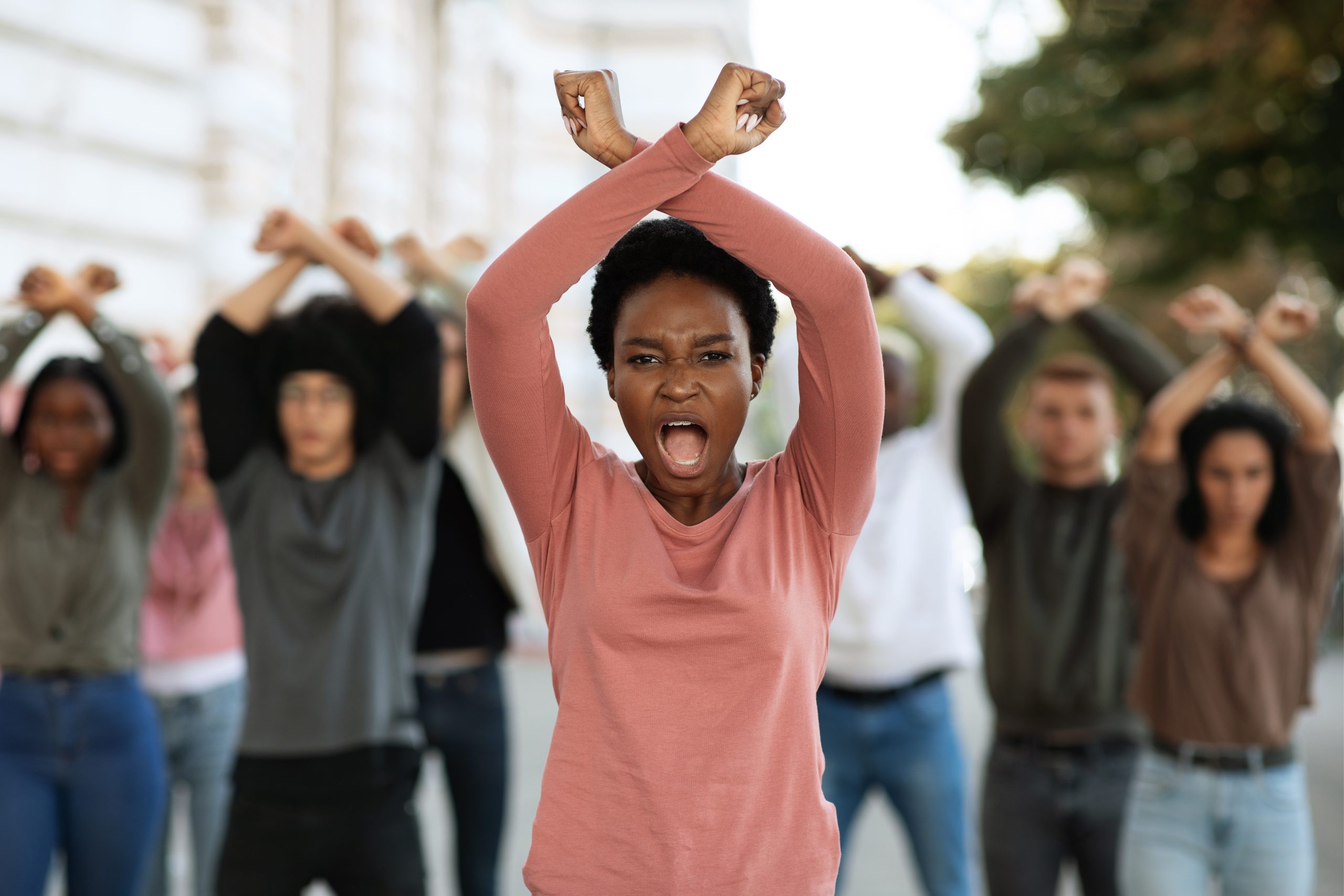 Angry black woman with clenched fists above her head protesting with multiracial group of people on the streets. International group of protestors making revolution, fighting for human rights
